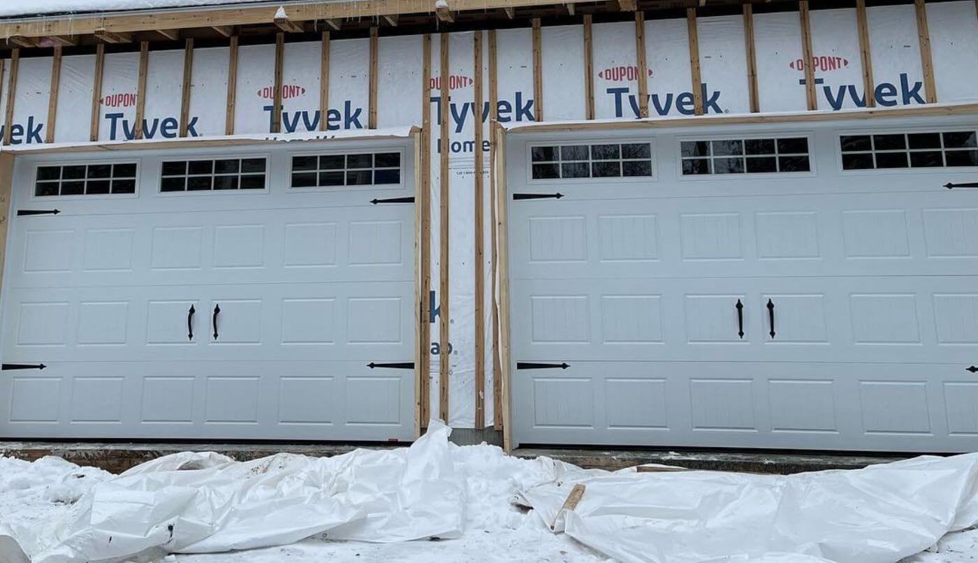 Deux portes de garage sont en train d'être installées sur une maison, représentant une étape de la construction.