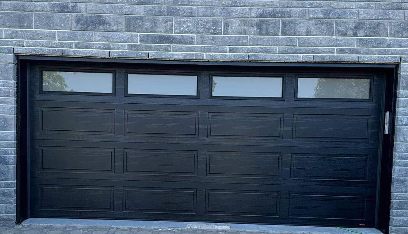 Porte de garage noire dotée de  fenêtres, alliant fonctionnalité et esthétique contemporaine.