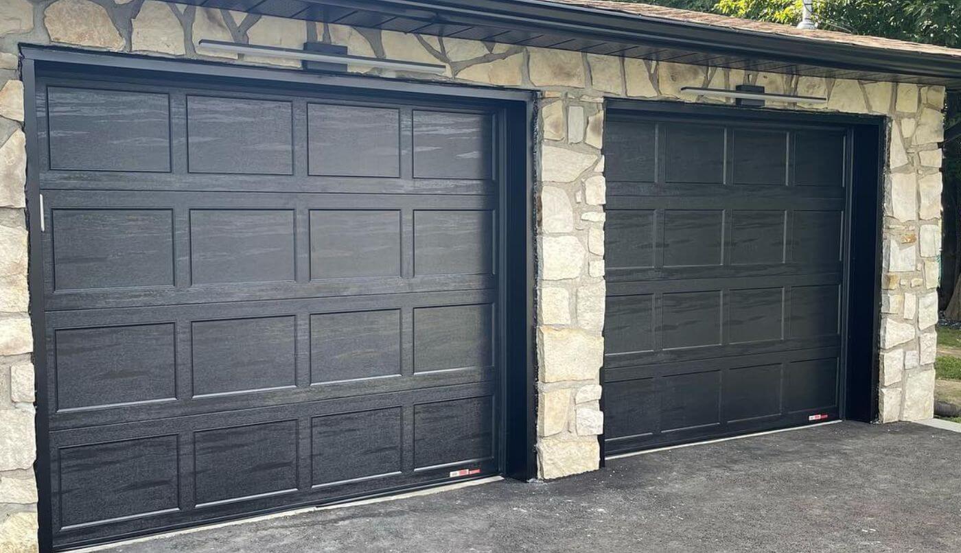 Deux portes de garage noires encadrées par un mur en pierre, créant un contraste élégant et moderne.