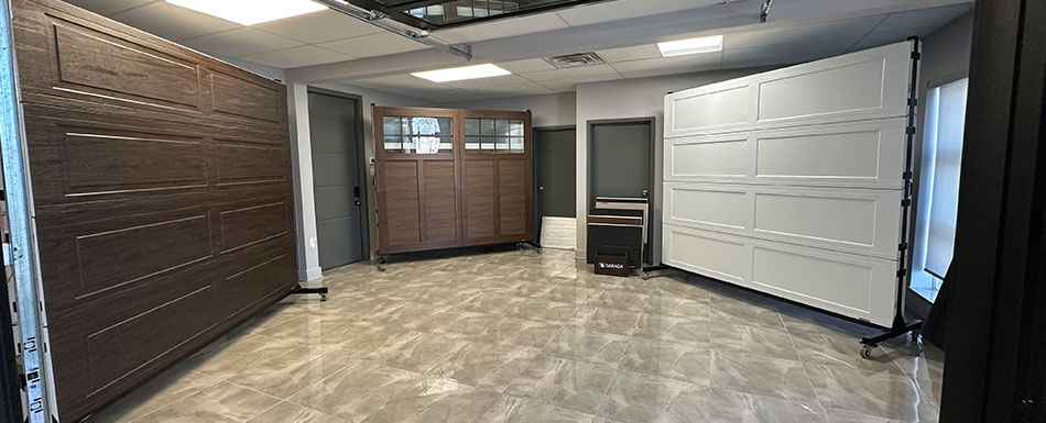 Salle de montre présentant divers modèles de portes de garage, incluant des designs vitrés, texturés et classiques, dans un espace moderne et lumineux.