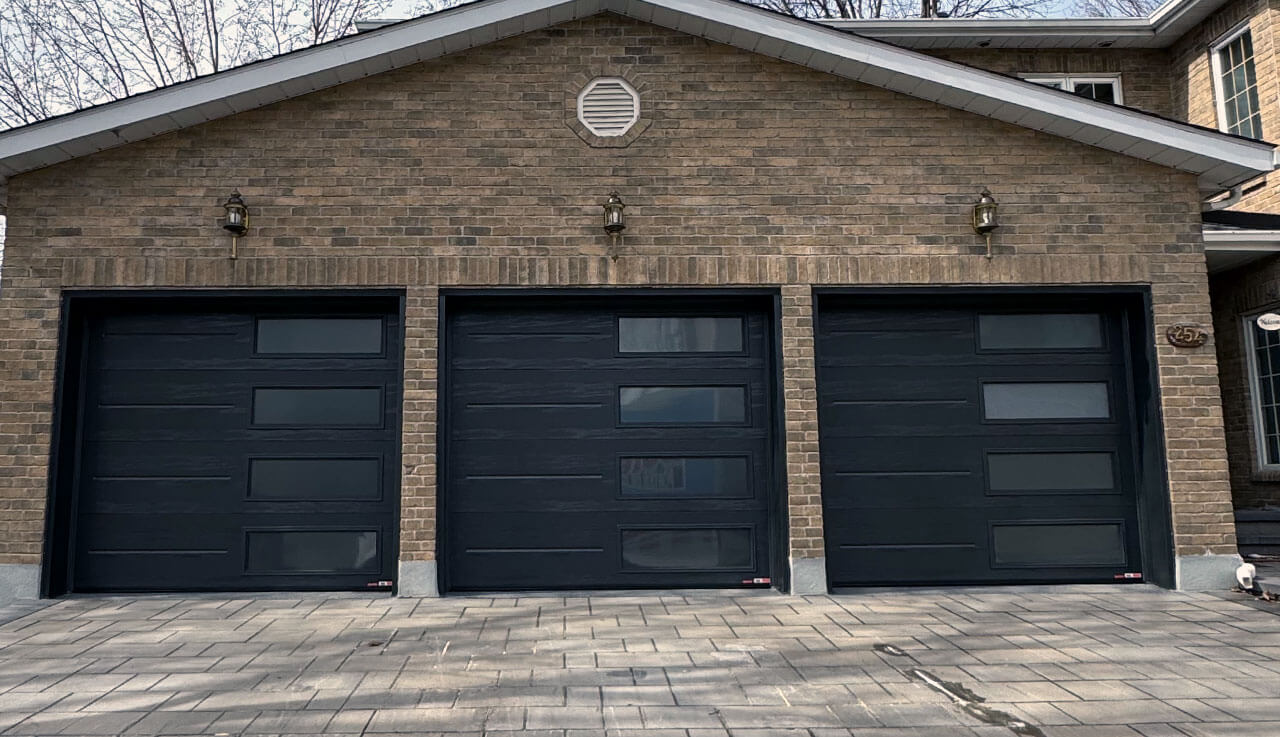 Trois portes de garage noires, sur un garage en briques, ayant chacune des fenêtres sur le côté.